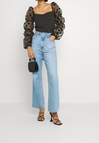 Top nero con maniche a sbuffo trasparenti a pois, abbinato a jeans a vita alta blu chiaro a gamba larga e sandali neri con tacco.