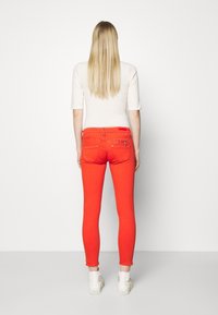 Rode skinny jeans met een gladde textuur, twee achterzakken en een tailleband met riemlussen. Gecombineerd met witte sneakers en een neutral top.