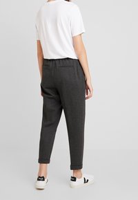 Grå, avsmalnande byxor med elastisk midja och bakfickor, parat med en vit t-shirt och vita sneakers med svarta detaljer.