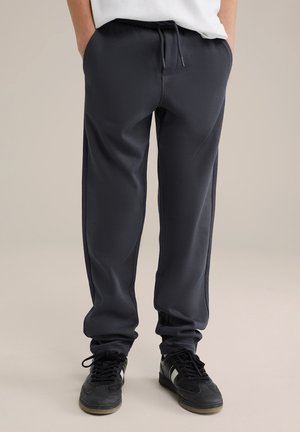 Donkergrijze sweatpants met een gestructureerde afwerking, voorzien van een elastische tailleband en een trekkoord. Zwarte sneakers met witte accenten maken de look compleet.