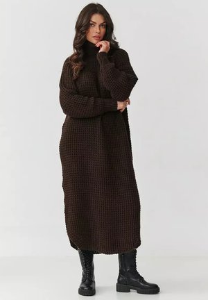 Brązowa dzianinowa sukienka maxi z wysokim kołnierzem, długimi rękawami i teksturowanym wzorem. Zestawiona z czarnymi sznurowanymi butami wojskowymi.
