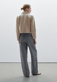 Cropped beige leather jacket with a smooth texture, paired with wide-leg gray pants in a lightweight fabric, worn with simple black sandals.