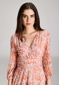 Kukallinen mekko vaaleanpunaisesta kankaasta, jossa on puffihihat, V-päällyste ja kokoontuva vyötäröyksityiskohta. Ominaisuutena värikäs kukkakuosi.