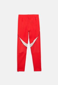 Κόκκινες αθλητικές κολάν με υφή, με λευκά τριγωνικά δ ιακοσμητικά και μαύρο piping κατά μήκος των ραφών. Ελαστική μέση και φερμουάρ στους καρπούς.