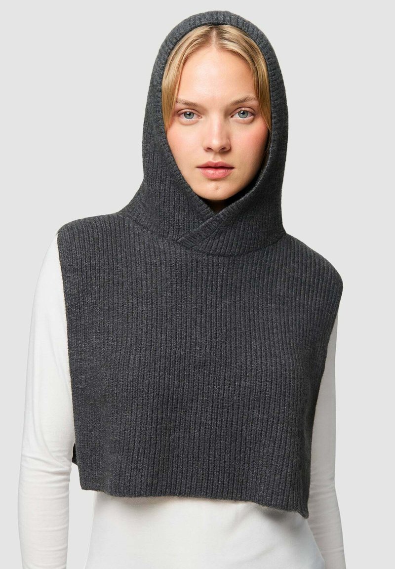 Hoodie senza maniche grigio a coste con collo alto e cappuccio. Tessuto morbido, design cropped, indossato sopra una maglietta a maniche lunghe bianca.