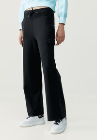 Svarta cargo-byxor med avslappnad passform, med sidfickor, dragsko i midjan och mjukt, slätt tyg. Bärs med vita sneakers.