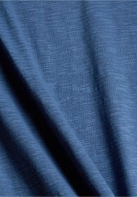 Modrý pletený materiál s jemným, texturovaným povrchem. Měkký, lehký a jemně se skládá, s nepatrnými barevnými variacemi.