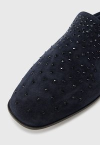 Μπλε ναυτικά μοκασίνια από σουέτ με στρογγυλεμένη μύτη, διακοσμημένα με μαύρες στρας που δημιουργούν υφή στην επιφάνεια της επάνω πλευράς.