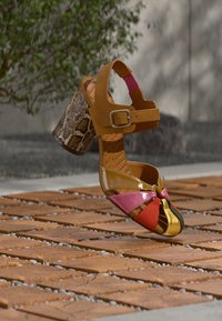 Πολύχρωμα σανδάλια με ψηλά τακούνια που διαθέτουν γυαλιστερό επάνω μέρος σε κίτρινες, ροζ και κόκκινες αποχρώσεις, καφέ λουράκι στον αστράγαλο και τακούνι με λεπτομέρεια σε σχέδιο δέρματος φιδιού.