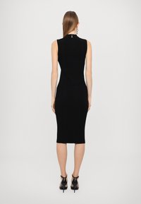 Rochie midi neagră cu model texturat, fără mâneci, având un decolteu rotund și un detaliu cu fermoar la spate. Purtați cu sandale negre cu barete.