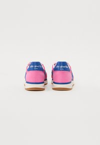 Chaussures de sport roses avec des accents bleus, présentant un talon en cuir lisse et un dessus texturé. Semelle douce avec une semelle extérieure en caoutchouc naturel.