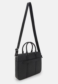 Sac à main synthétique noir avec une bandoulière réglable, doubles poignées, fermeture éclair, extérieur à motifs et détail de logo en relief à l'avant.