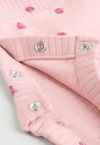 Gros plan sur un tissu en maille côtelée rose avec des boutons-pression métalliques et des cœurs rose foncé dispersés sur le textile.
