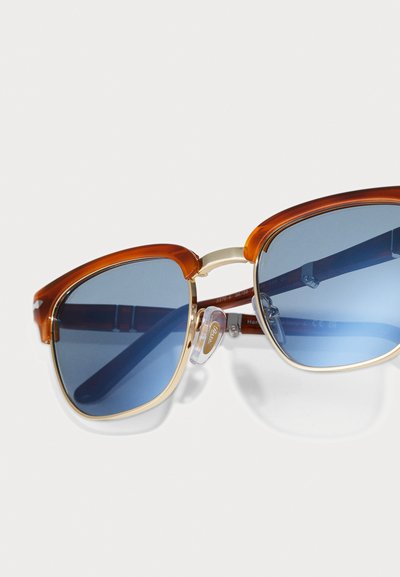 Ochelari de soare cu un cadru lat și unghiular, realizat din acetat de culoare chihlimbar și lentile albastre, accentuați cu accesorii din metal aurit și pernuțe nazale transparente.