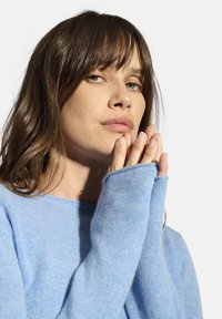 Hellblaues Sweatshirt mit langen Ärmeln und Rundhalsausschnitt. Der Stoff erscheint weich und leicht fusselig und verfügt über Daumenlöcher in den Bündchen.