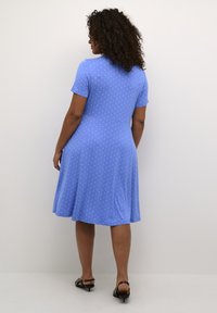 Blå kortærmet kjole med hvide prikker, flagrende design, knæ-længde, lavet af strækbart stof og rund halsudskæring.