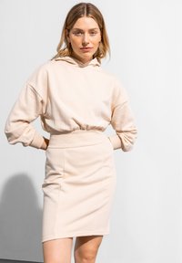 Beige Baumwoll-Hoodie mit Kordelzug und gerippten Bündchen, kombiniert mit einem taillierten beige Minirock, der eine glatte Textur und ein schlichtes Design zeigt.