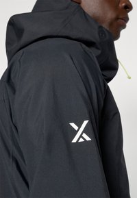 Zwarte waterdichte jas met een hoge kraag, verstelbare capuchon en een wit logo op de linkermouw. Gladde textuur, minimalistisch ontwerp.