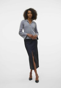 Gilet gris zippé avec des manches évasées, associé à une jupe midi fendue noire. Textures lisses, design ajusté et couleurs unies.