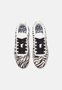 Sapatilhas com padrão de zebra em preto e branco, design de atacadores, colarinho almofadado e sola de borracha. Tecido texturizado para um interesse visual.
