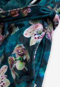 Dark teal fabric with a tied knot detail and a floral pattern featuring pink and green orchid-like flowers.