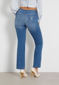Jeans in denim di color azzurro chiaro con un design a gamba dritta, dotati di due tasche posteriori con una piccola decorazione a triangolo. Abbinati a tacchi alti bianchi.