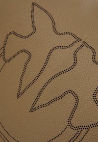Contour d’un oiseau et formes abstraites créées par de petites perforations sur une surface en cuir brun texturé.