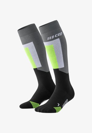 Kompressionsstrümpfe in Schwarz, Grau und fluoreszierendem Grün. Mit geometrischen Mustern und strukturierten Akzenten. Knielanges Design für Unterstützung.