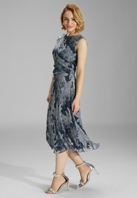 Vestido azul con estampado floral, con un cuerpo ajustado y un dobladillo acampanado. Hecho de una tela ligera, combinado con unos tacones metálicos con tiras.