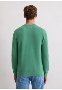 Grüner Strickpullover mit strukturiertem Muster, Rundhalsausschnitt und langen Ärmeln, kombiniert mit hellblauen Jeans aus Denim.