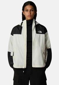 Lekka, dwukolorowa kurtka z kremowym tułowiem i czarnymi rękawami, z zamkiem błyskawicznym z przodu i logo na górnej lewej stronie.