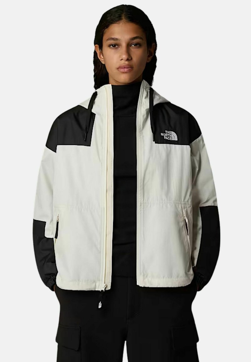 Lekka, dwukolorowa kurtka z kremowym tułowiem i czarnymi rękawami, z zamkiem błyskawicznym z przodu i logo na górnej lewej stronie.