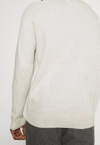 Světlě šedý pletený svetr s žebrovanou texturou, dlouhými rukávy a kulatým výstřihem. Lem a manžety jsou zakončeny hladkým pletením.