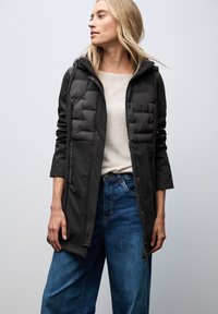 Black puffer jacket with a hood, featuring quilted front panels, zippered pockets, and long sleeves, paired with loose blue denim pants.