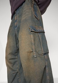 Cargo kalhoty v bledě modrém denimu, se širokými bočními kapsami, volným střihem a kontrastním švem. Tkanina s texturou a jemným opotřebením.