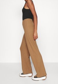 Pantalon large côtelé beige avec taille élastique, associé à un haut sans manches noir et des baskets à semelle épaisse.