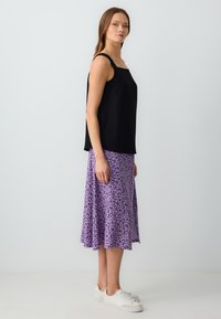 Top senza maniche nero abbinato a una gonna a fiori viola, che presenta una vestibilità rilassata e una superficie in tessuto liscia. Indossate sneakers bianche.
