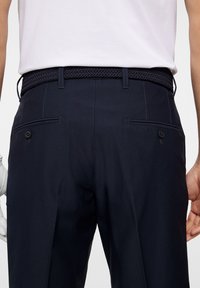 Marina golfbyxor med en slät textur, utrustade med ett flätat bälte, två bakfickor och kontrasterande sömdetaljer.