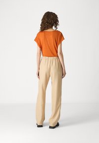 Haut orange à manches courtes avec une coupe ample, associé à un pantalon en mélange de lin beige avec taille élastique et design jambes droites.