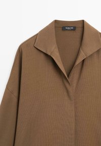 Brown, textured shirt with a pointed collar, long sleeves, and front button closure. Features a minimalist design and soft fabric.