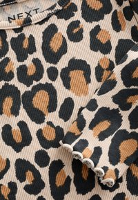 Tissu imprimé léopard en beige, noir et marron avec une texture côtelée. Présente un col arrondi et des bords en dentelle aux manches.