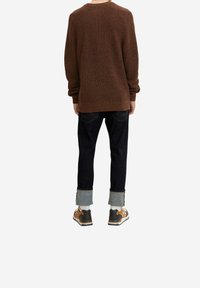 Maglione lavorato a maglia marrone, jeans in denim scuro con risvolti, e scarpe marroni e nere con calzini bianchi, visti da dietro.