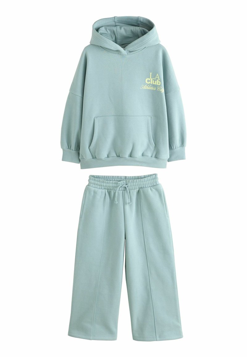 Hellgrüne Kapuzenjacke und passende Sweatpants aus weichem Material. Die Kapuzenjacke hat eine große Fronttasche und ein Logo. Die Hose verfügt über einen elastischen Bund.