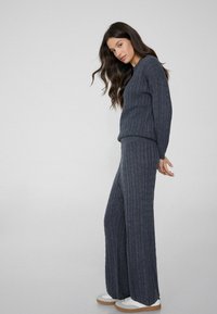 Donkergrijze ribgebreide trui en wijde broek outfit, met een textuurstof en een relaxte pasvorm, gecombineerd met witte sneakers.