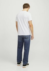 Weißes T-Shirt mit kurzen Ärmeln aus Baumwolle, kombiniert mit lockeren blauen Jeans. Die Schuhe sind schwarz-weiße Sneaker.
