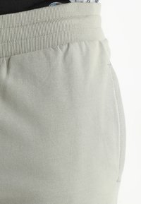 Pantalons de survêtement gris clair avec une taille élastique, texture douce, poches latérales et couture discrète le long des coutures.