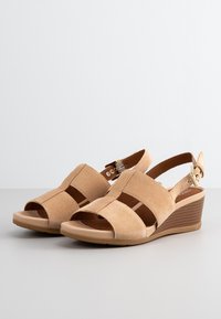 Beige semišové sandály na klínu s otevřenou špičkou, s křížovými řemínky a boční sponou. Texturovaný klín s hnědým vertikálním pruhovaným vzorem.