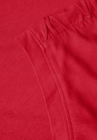 Tissu rouge avec une texture en fines côtes. Les bords présentent des détails froncés, mettant en valeur une couture lisse. La vue en gros plan met en évidence la douceur du matériau.