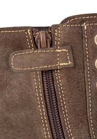Botte en daim marron avec une fermeture éclair marron foncé fermée, des coutures beige et une sangle traversant la fermeture près des œillets métalliques sur le côté droit.