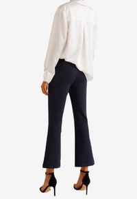 Witte blouse met lange mouwen en een kraag, gecombineerd met marineblauwe flared pants en zwarte hoge hakken met enkelriemen. Gladde stoffen texturen.